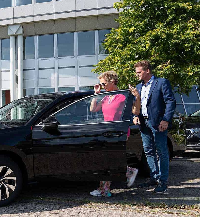 Eine Dame steigt in einen VW vor Firmengebäude ein. Arndt-Mitarbeiter steht daneben | Arndt Auto-Abo fürs Gewerbe