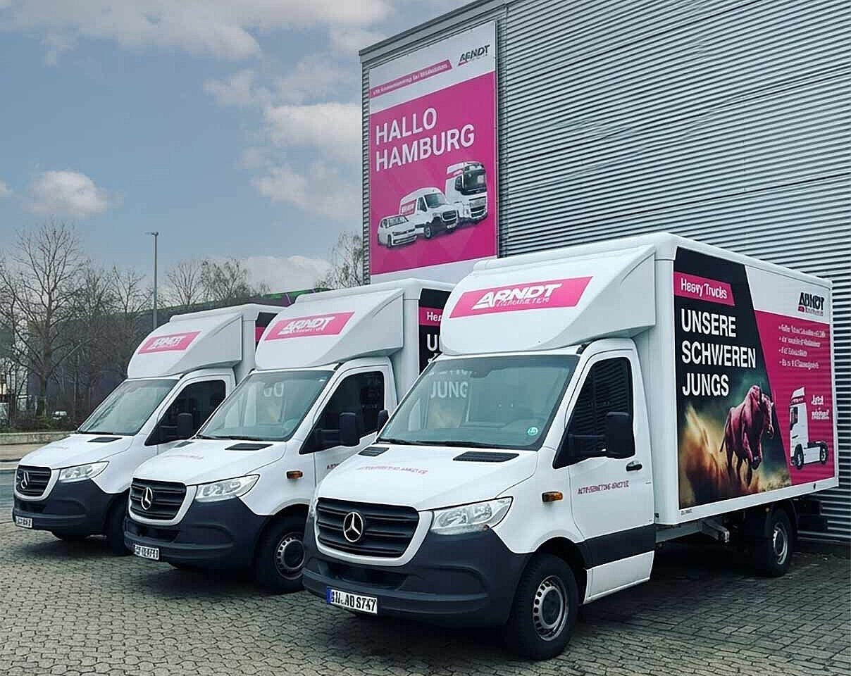 Drei Mercedes Transporter Koffer mit Arndt Branding auf dem Parkplatz vor „Hallo Hamburg“ Poster – Transporter mieten in Hamburg