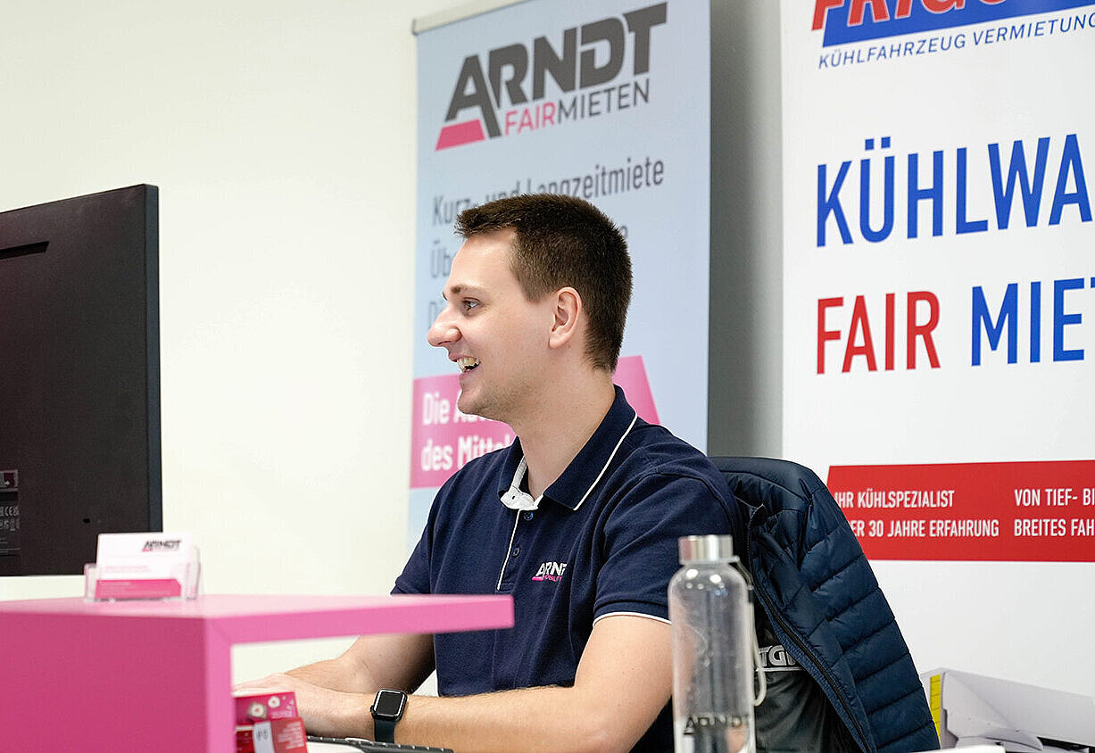 Sympathischer junger Mitarbeiter sitzt am Computer in einer Station der Autovermietung Arndt