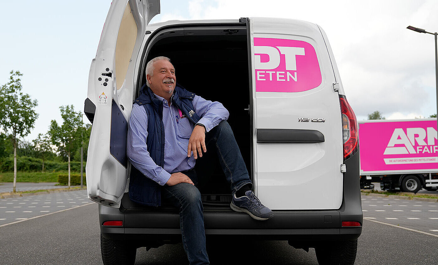 freundlicher Mitarbeiter der Autovermietung Arndt sitzt bei geöffneter Sprintertür halb im Laderaum des Sprinters