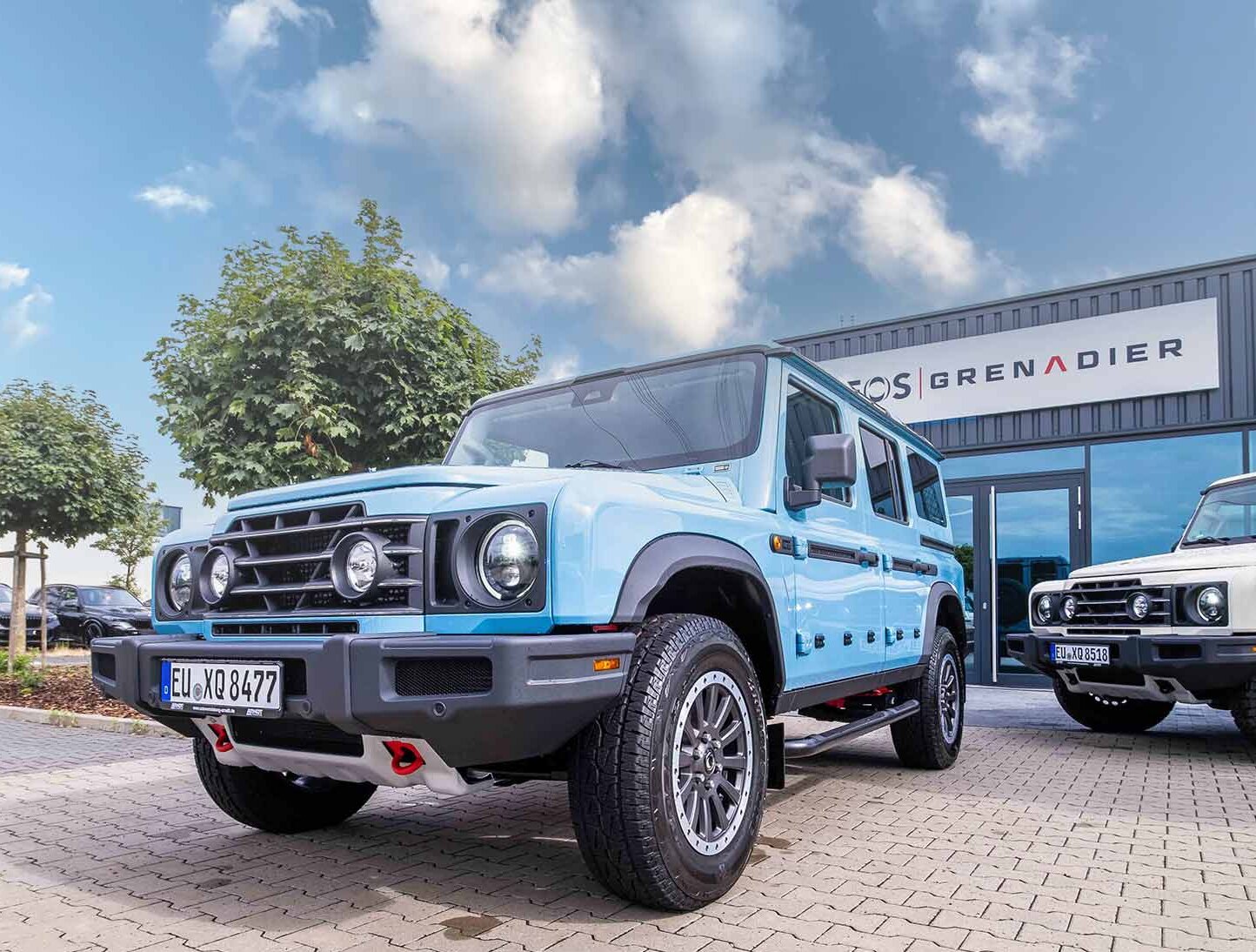 Blauer Ineos Grenadier vor einem Autohaus | Autovermietung Arndt