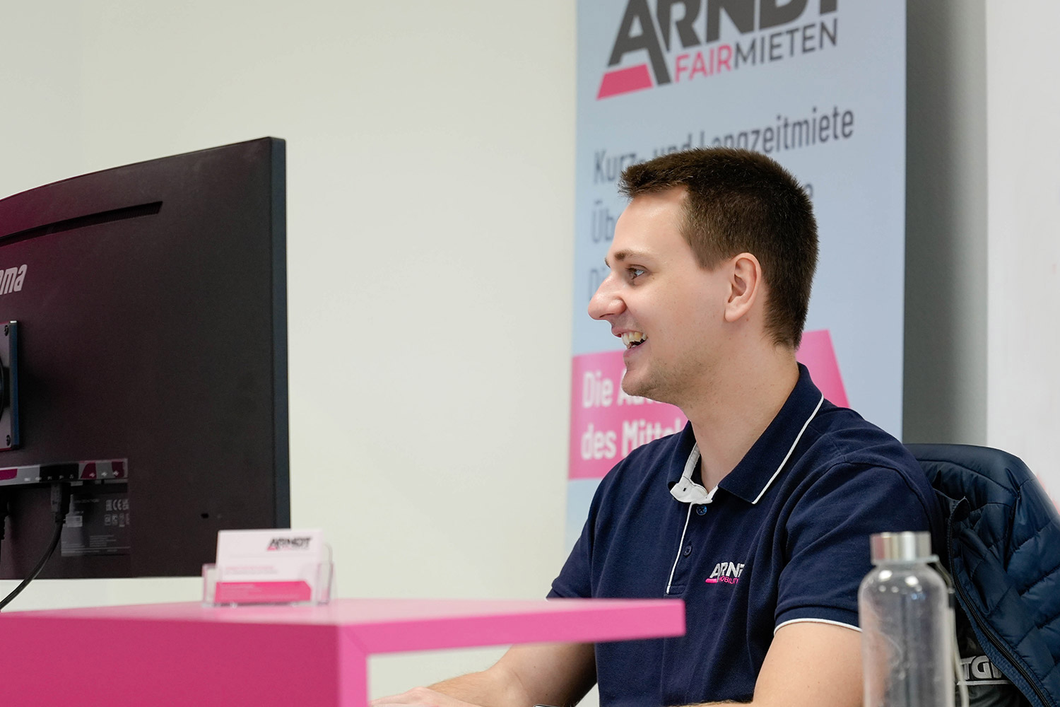 Ein freundlicher Stationsmitarbeiter sitzt am Computer in der Niederlassung der Autovermietung Arndt